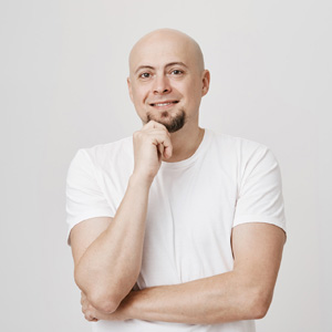 Portrait of handsome bald european male touching his beard while smiling and thinking about something with crossed hand, wearing white t-shirt and standing over gray background. Emotions concept
